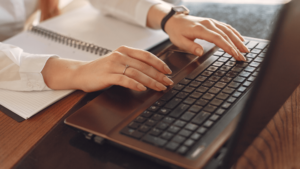 Kobiece dłonie na klawiaturze laptopa piszące wpis blogowy na temat budowania Trwałych Relacji Newsletter Vs Blog - Co Wybrać